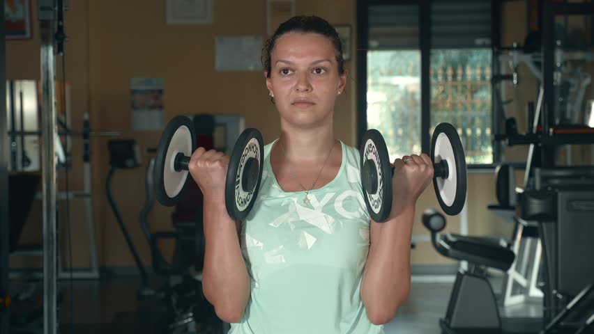 Young woman lifting weights with arms in gym.