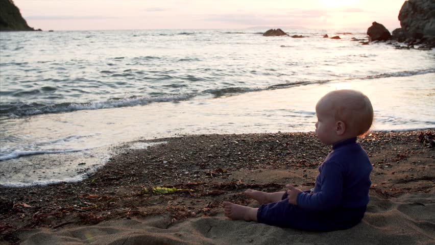 Cute caucasian 1,5 years old boy is looking at splashing sea waves on the beach and playing with sticks. Ritz bay, Nakhodka, Russia. September evening