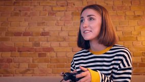 Closeup portrait of young cheerful girl playing video games using the game console entertaining sitting on the couch in a cozy apartment indoors