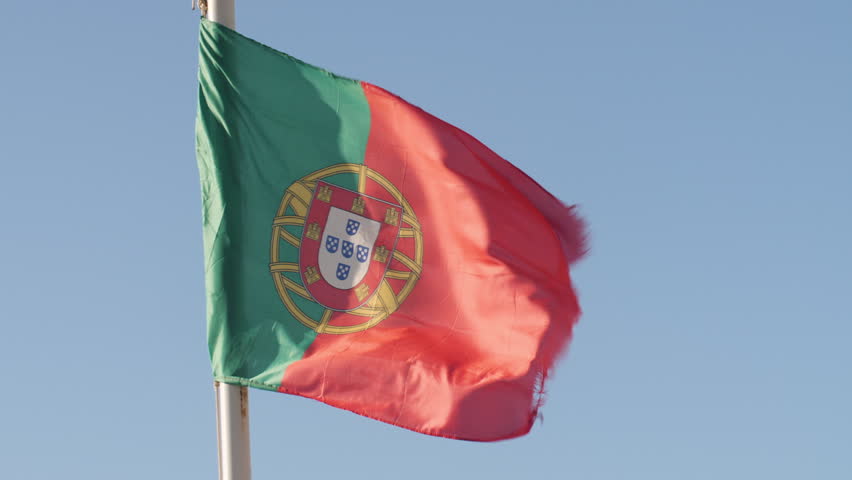 Shot of Portugal national flag under a blue sky, in slow motion.