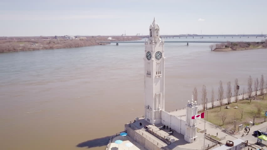 Cinematic drone / aerial footage rotating showing the Clock Tower of the Old Port (Vieux Port) of Montreal and Jean Drapeau Park on the background during fall season.