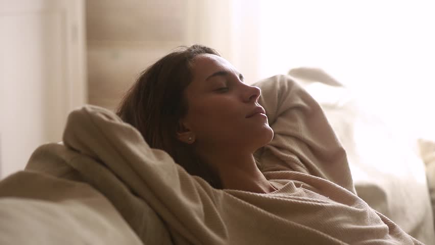 Calm young woman having healthy daytime nap dozing relaxing on couch with eyes closed hands behind head, peaceful girl sleeping breathing fresh air resting leaning on comfortable sofa at home | Shutterstock HD Video #1029331790
