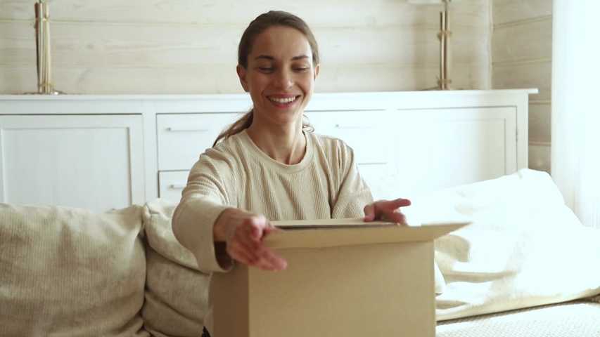 Excited young woman consumer open cardboard box get postal parcel, happy female customer receive carton package with gift sit on sofa at home satisfied with fast shipment online purchase delivery | Shutterstock HD Video #1029331811