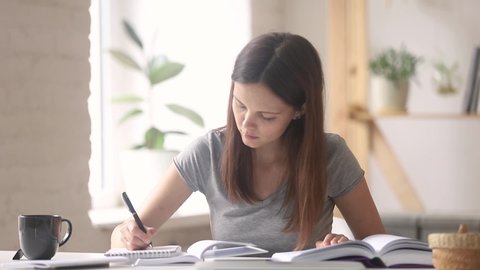 Serious woman student girl reading turn pages of textbook makes notes in notebook, learning doing task preparing for examination sitting at desk at home or high school class, education process concept