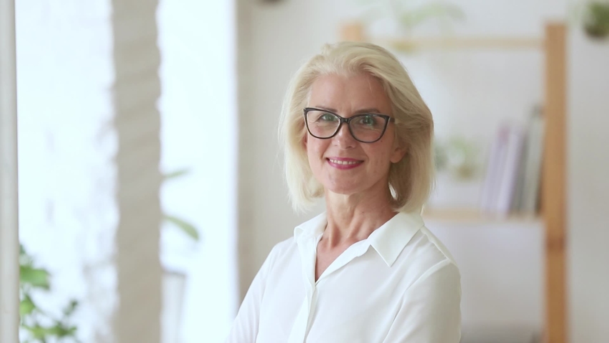 Head shot of fifty years woman wearing glasses pose in office room looking at camera laughing feels happy, independent elderly company owner, coach or leader successful businesswoman portrait concept | Shutterstock HD Video #1029333209