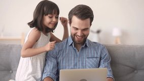 Father and little daughter having fun at home sitting on couch kid girl kiss on cheek dad listens music online use laptop app watching video clip dancing moving feels happy, weekend activities concept