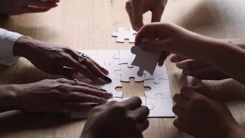 Side view hands of united diverse people taking part assembling white jigsaw puzzle, different ethnicity friends put pieces together search common solution, help support teamwork and synergy concept