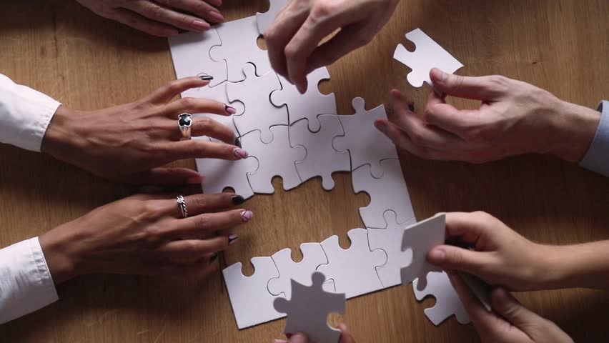 Above close up view hands multi-ethnic business people teammates connects together white pieces of jigsaw puzzle on office desk, participating team building activity, search solutions, synergy concept Royalty-Free Stock Footage #1029333326