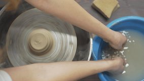 A close up video of pottery making process. A skilful master / potter in moulds / shapes the clay and helps his student who cleans his hands in the water. The background is blurred.