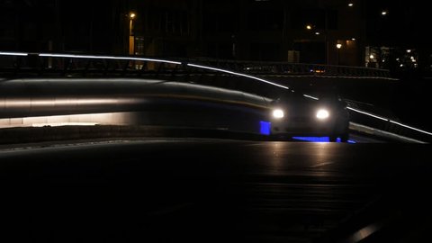 Brussels, Belgium - April 1, 2019:Wonderful view of a well-lit modern highway with metallic road fence and steeply inclined surface and rushing cars with switched headlights at night