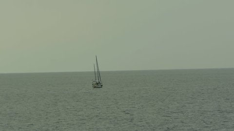 A sailboat on the open sea off the coast of Malta. Calm Mediterranean sea and a gray sky give a lonely feel to the scene. Wide angle view.