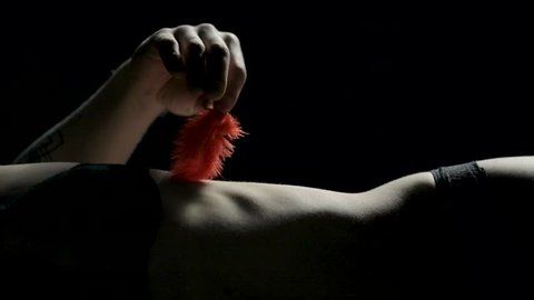 A male hand slowly tickles a lingerie wearing female body with a red feather