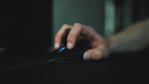 Close up of hand of gamer playing in the video game at night time using mouse