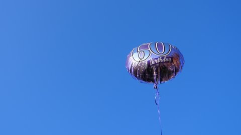 60th birthday anniversary helium balloon is flying slowly against blue sky background on the right side of the frame, copy space.