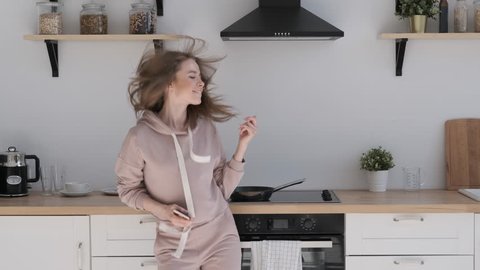 Happy freelancer woman glad to receive new pay. Girl enjoys good news. Beautiful girl dancing in the kitchen with the phone in hand