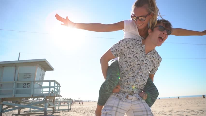 Piggy back at the beach. Young couple having fun at Santa Monica beach Los Angeles. Slow motion 