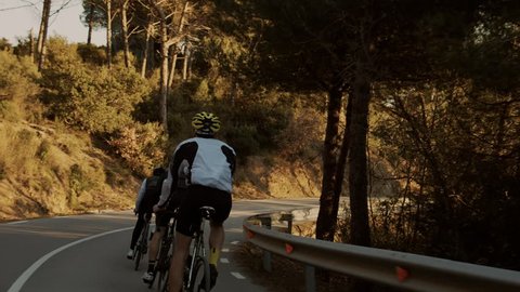 Two professional or amateur cyclists descend down mountain curvy road during golden hour sunset. Beautiful image of healthy sport lifestyle, romantic and dreamy view on excercise