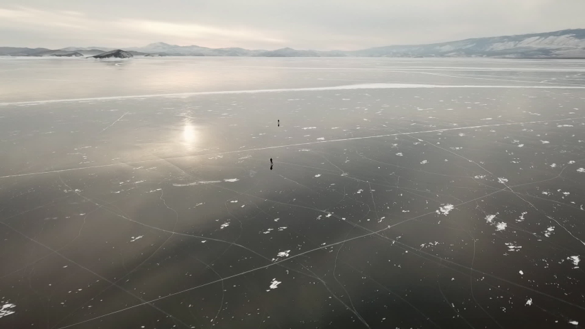 People tourist walk go on smooth surface. Picturesque Lake Baikal Cracks blue glossy clear ice hummocks snow snowdrifts. Best North Russia Asia. Winter sunny day blue sky. Aerial Approach.