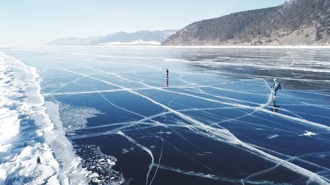 People tourist walk go on smooth surface. Picturesque Lake Baikal Cracks blue glossy clear ice hummocks snow snowdrifts. Best North Russia Asia. Winter sunny day blue sky. Aerial Approach.