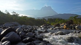 Early morning scenery with fresh water river flowing over rocks and Mount Kinabalu in background. Video, 4K. 