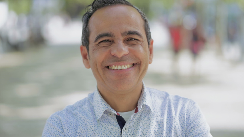 Cheerful mature man smiling at camera outdoor. Portrait of handsome Hispanic man standing with hand on chin and laughing. Emotion concept | Shutterstock HD Video #1029374822