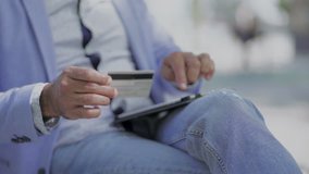 Man using tablet pc and holding credit card. Cropped shot of middle aged man sitting on bench and shopping online with digital tablet and credit card. E-commerce concept