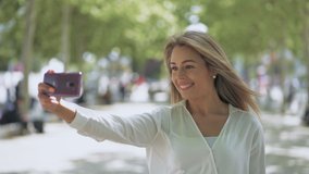 Attractive smiling girl taking selfie outdoor. Beautiful happy young woman taking selfie with smartphone on street. Taking picture concept