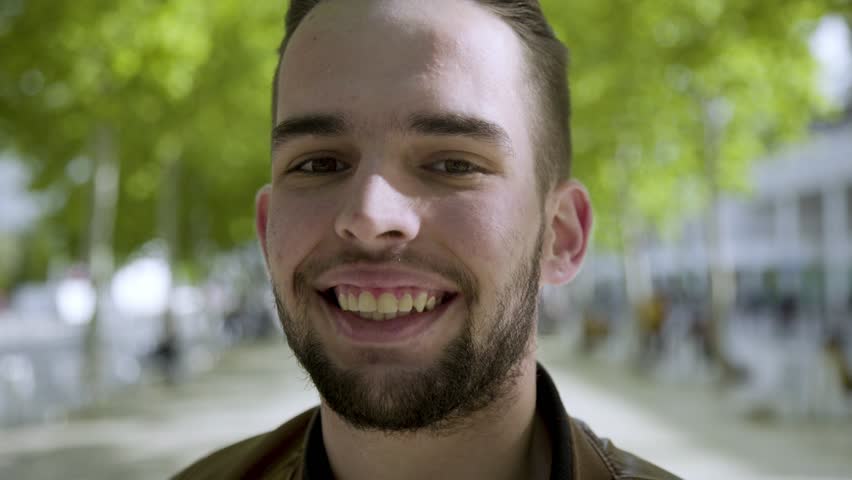 Closeup shot of smiling young man winking while looking at camera. Handsome young brunet flirting outdoor. Concept of flirt