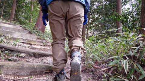 A slow motion shot of a female hiker climbing stairs on a rural mountain trail in japan.