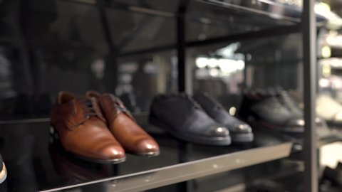 A close-up of a male costumer taking classic style dark blue pair of shoes from a glass display of goods in luxury business fashion store. Approaching camera shot