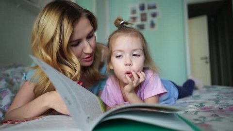 Kid kissing mother. A young loving mother reads bedtime stories to her little beautiful daughter, who goes to bed in her bed. learn a foreign language with a child