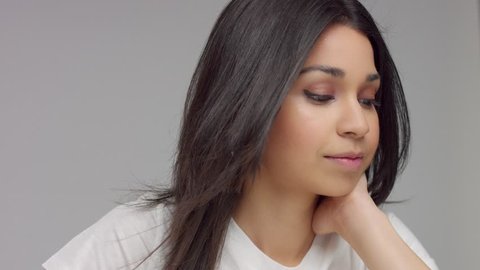 young mixed race woman in studio watching down showing eye makeup and turn her head. Slowmotion blowing hair
