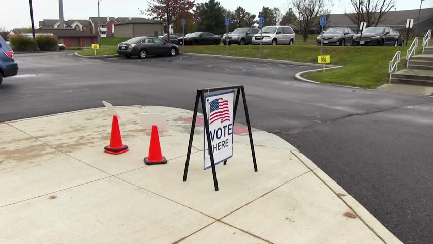 Vote here sign with American flag blowing in the wind, wide
