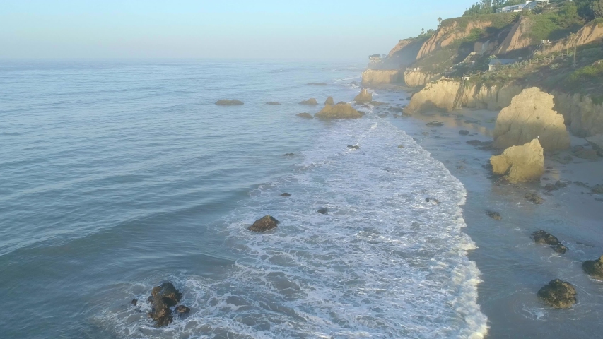 Aerial shots of El Matador beach over breaking waves and rocks on a hazy summer morning in Malibu, California
