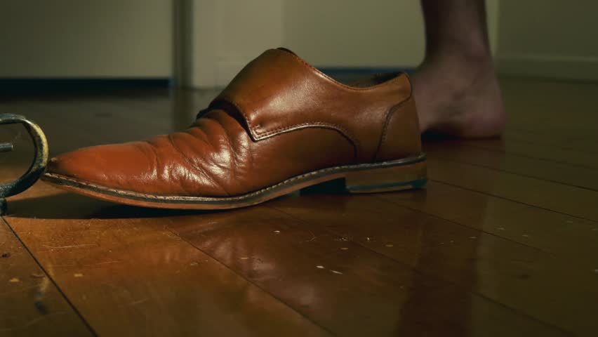 A low shot video of good looking brown leather shoes being wiped and placed next to the other one with classy old school cinematic color grade.