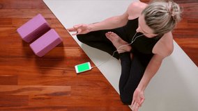 Top view of young woman sitting down on Yoga mat with Smartphone and Earphones meditating, legs crossed in Half Lotus Pose.
