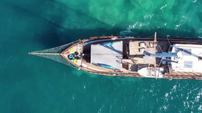 Aerial birds eye drone view video of beautiful wooden sailboat cruising in deep blue sea of Mykonos island, Cyclades, Greece