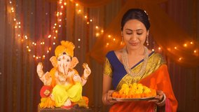 Beautiful Indian woman with flowers on pooja thali - celebrating Ganesh Chaturthi. Festival concept. Indian stock video of a middle-aged woman preparing for pooja wearing a saree