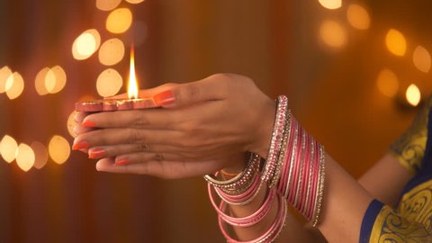 Beautiful hands of an Indian woman wearing bangles - holding a diya. Diwali Festival. Indian stock footage of daughter-in-law of the family lighting a diya and holding with both hands