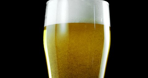 Close-up of glass of beer against black background. Bubbles and foam in beer glass.  स्टॉक वीडियो