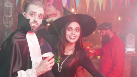 Young people drink and dance at a halloween party in a local pub. Gang of friends dancing and having fun diguised in scary costumes.