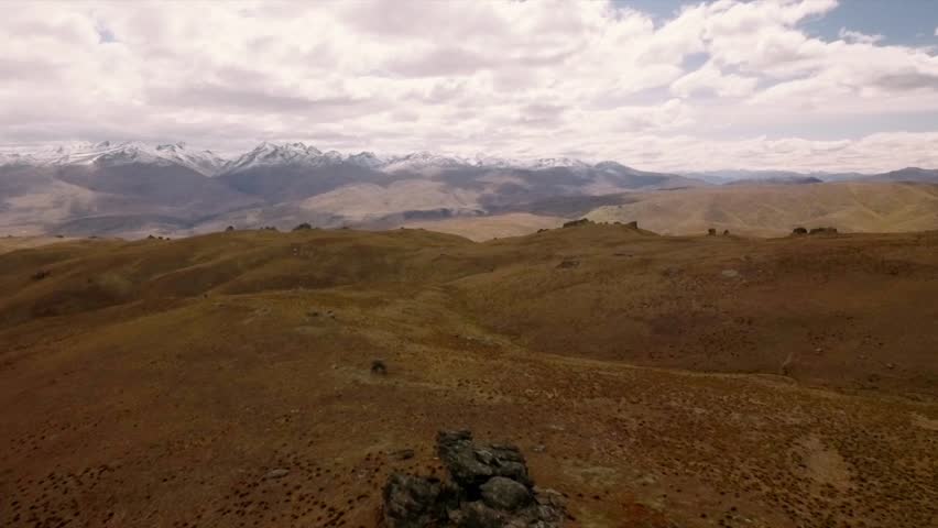 Barren landscape of central Otago in New Zealand on summer day. Snowy peaks of Southern Alps on the horizon. Aerial footage.