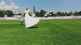 aerial video, view from the top, in the stadium, in the center of a green football field, newlyweds in wedding attire dancing, spinning. spring sunny day. wedding