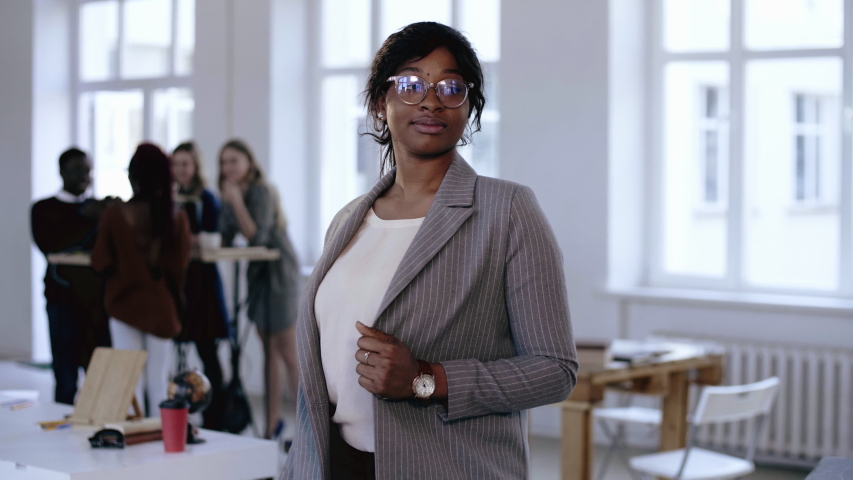 Happy professional young black CEO business woman in formal suit, eyeglasses posing, smiling at modern light office.