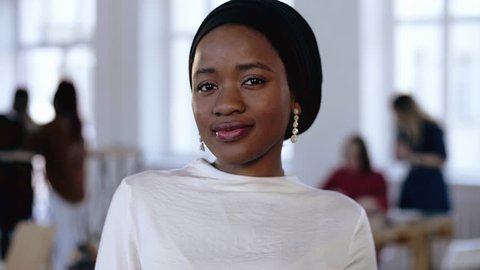 Young professional successful African entrepreneur woman wearing ethnic head wrap smiling modestly at modern office.