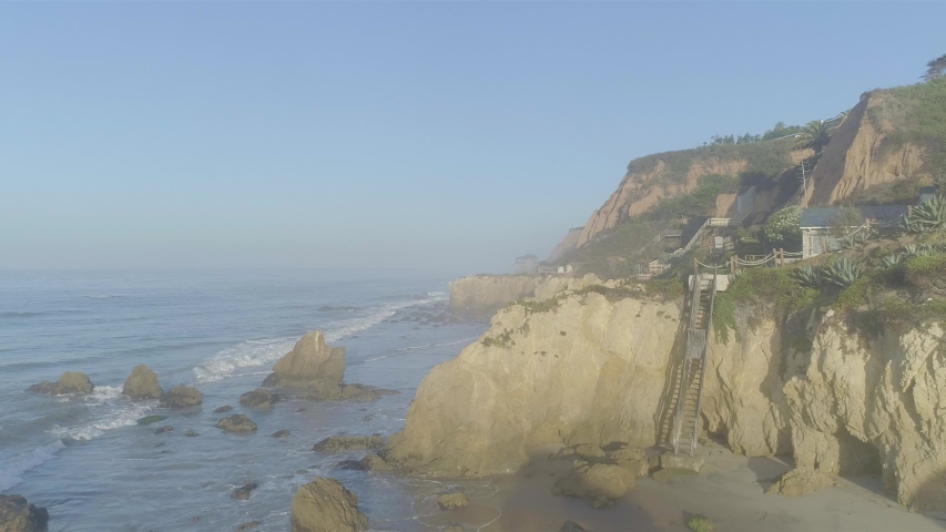 Aerial shots of El Matador beach over breaking waves and rocks on a hazy summer morning in Malibu, California