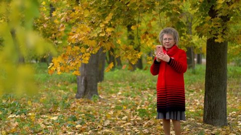 woman in red coat dials a phone number under a tree in autumn park