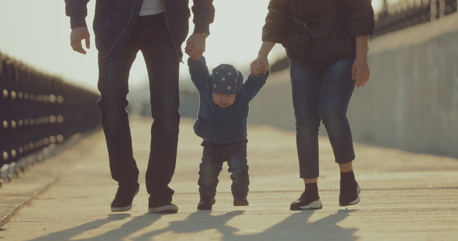Little boy walks with his parents. Mom and Dad hold the baby by the handles and walk along the path. Bottom view.