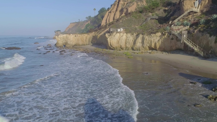 Aerial shots of El Matador beach over breaking waves and rocks on a hazy summer morning in Malibu, California