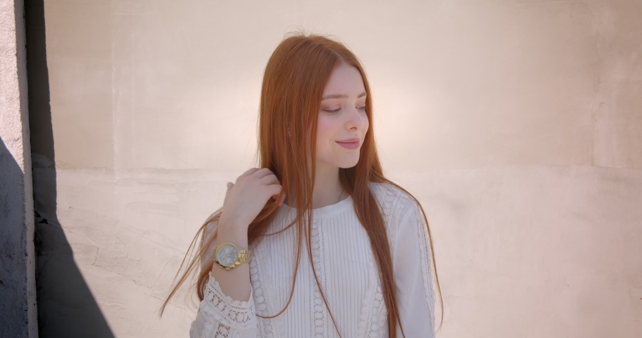 Pretty ginger model posing smilingly into camera on white wall background.